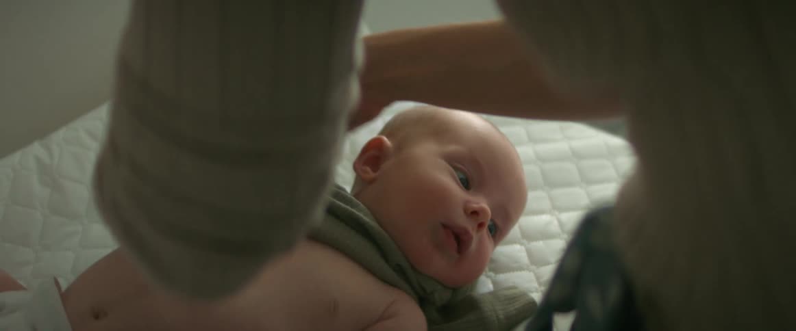 A mother putting clothes on her baby who lays on a changing pad