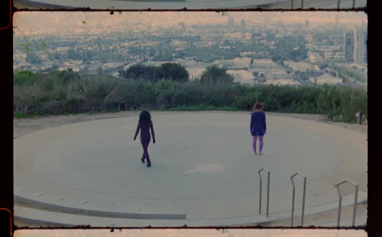 Two women dressed in purple walking in a circle at observatory over city skyline
