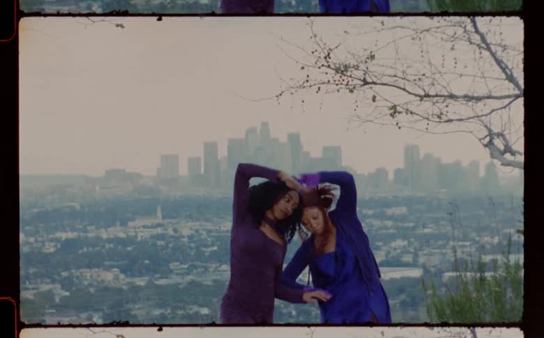 Female dancers wearing blue and purple dresses dances against city silhouette in the mist