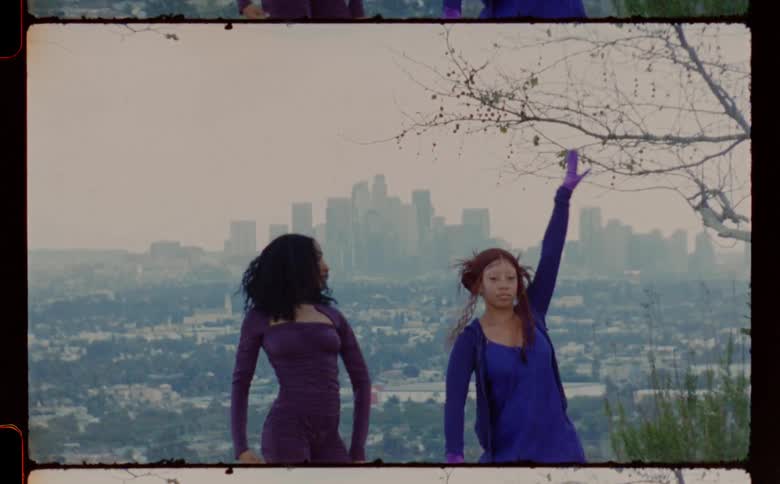 Two female dancers perform routine on hill overlooking foggy cityscape