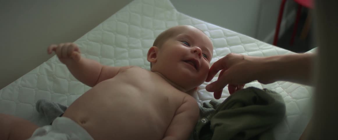 Baby lying on its back smiles as mother caresses the child on the cheek