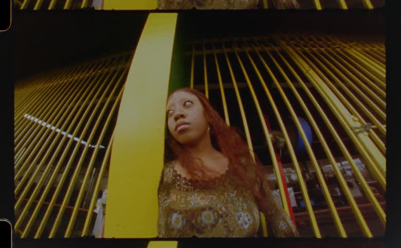 Young woman reclined on a column in front of a yellow railing looking at the camera