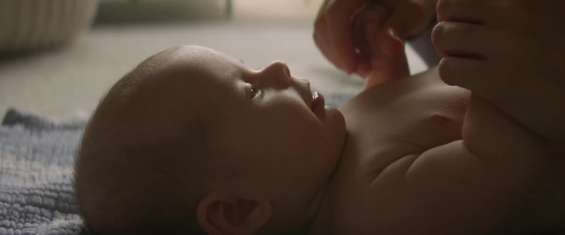 Mother plays with smiling baby on floor during the day holds hands and boops nose