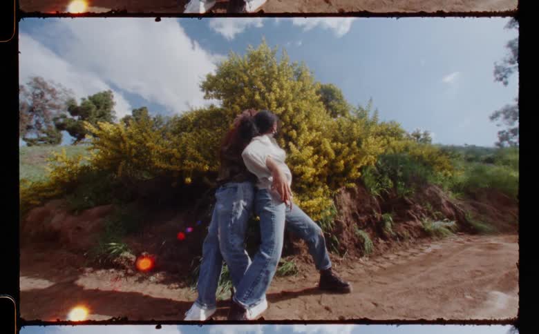 Two women dancing together in front of a yellow plant