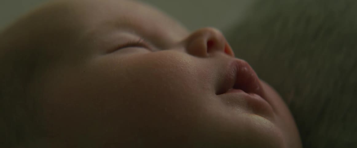A newborn baby moves their lips as they sleep