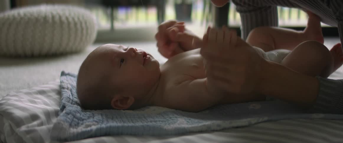 Happy baby wiggles and moves his arms while resting on the floor next to his mother at home