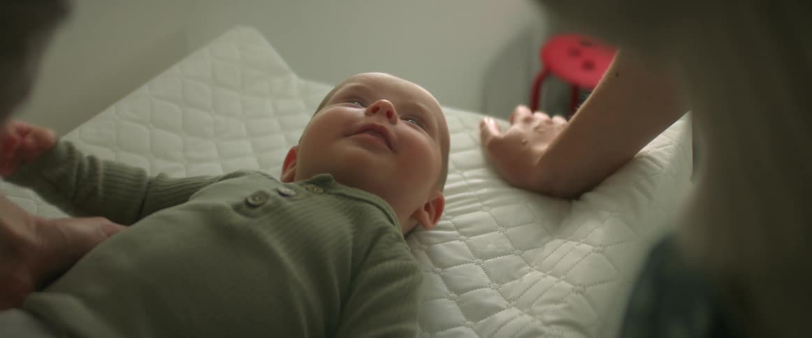 Mother leans over baby lying on a thin quilted mattress
