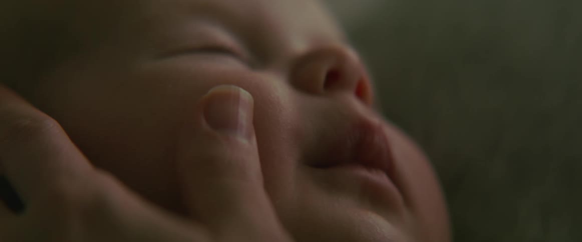 A woman has her hand on her babys face rubbing their cheek with her thumb