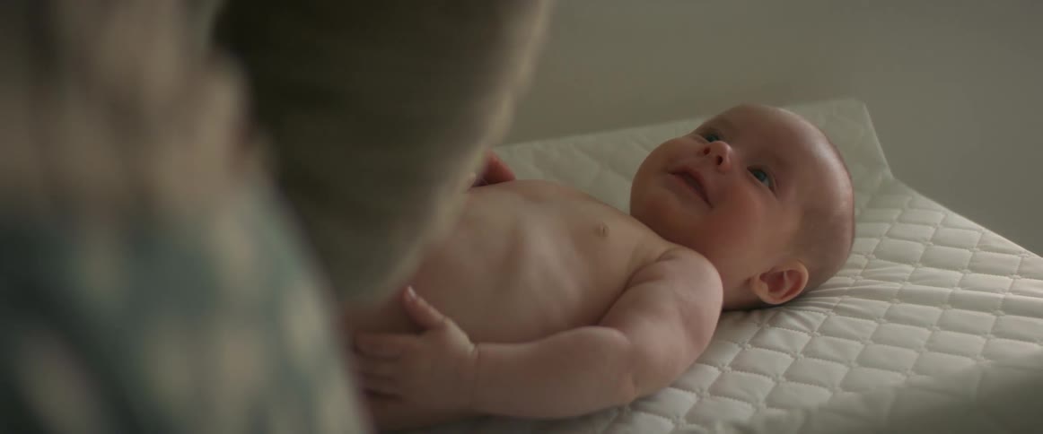 A baby is laying on a changing table smiling up their mother with an excited expression as the mother gently rubs the babies chest