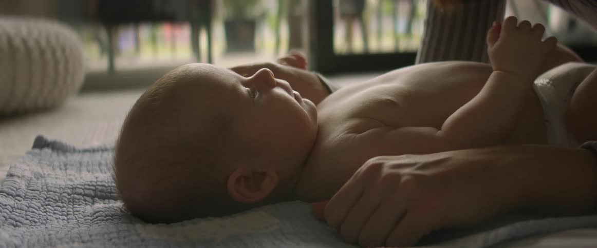 A baby is lying on a blanket on the floor looking up at their mother