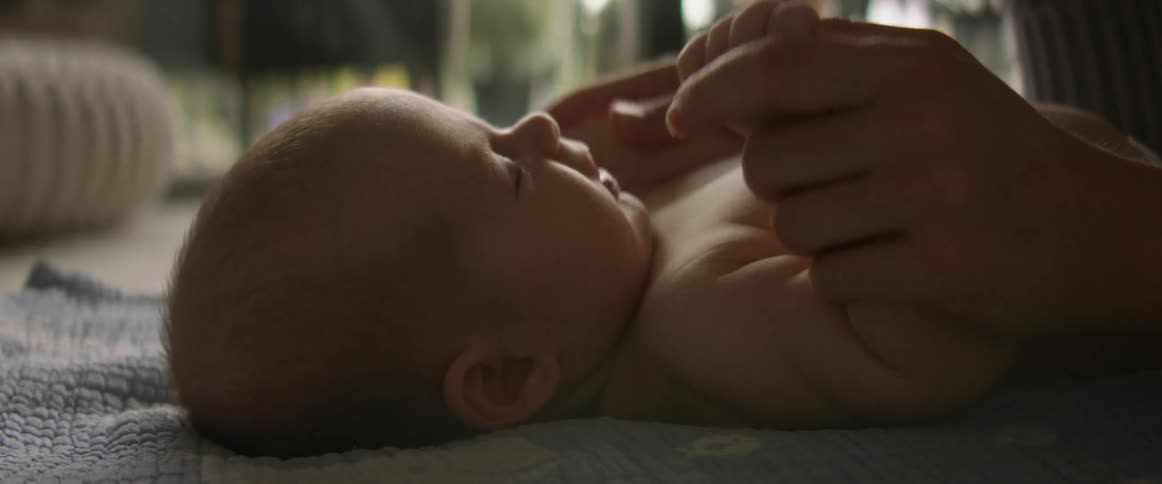 A baby lays on the floor while an adult plays with him