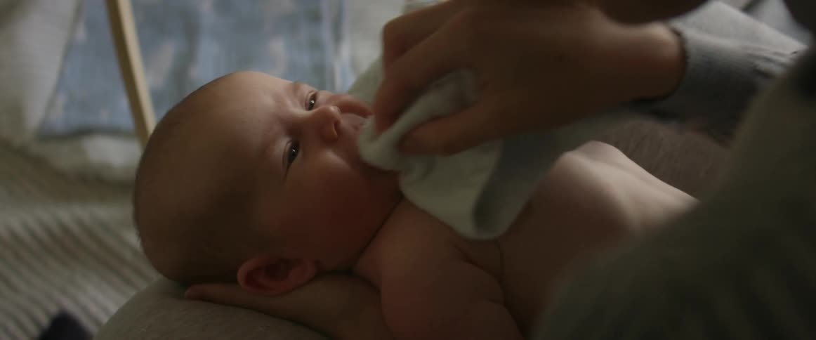 A woman is wiping her babys face with a cloth as they smile and lift their arms