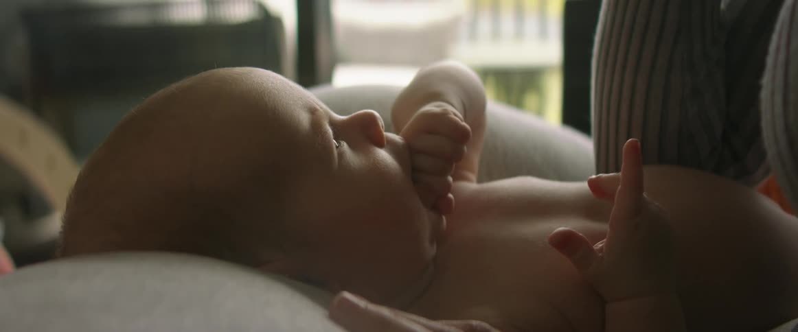 Mother holds child on her lap while the child sucks on a small hand