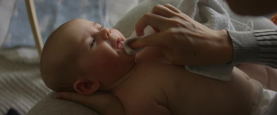 Mother holds hand under baby and wipes drool form childs face with a towel