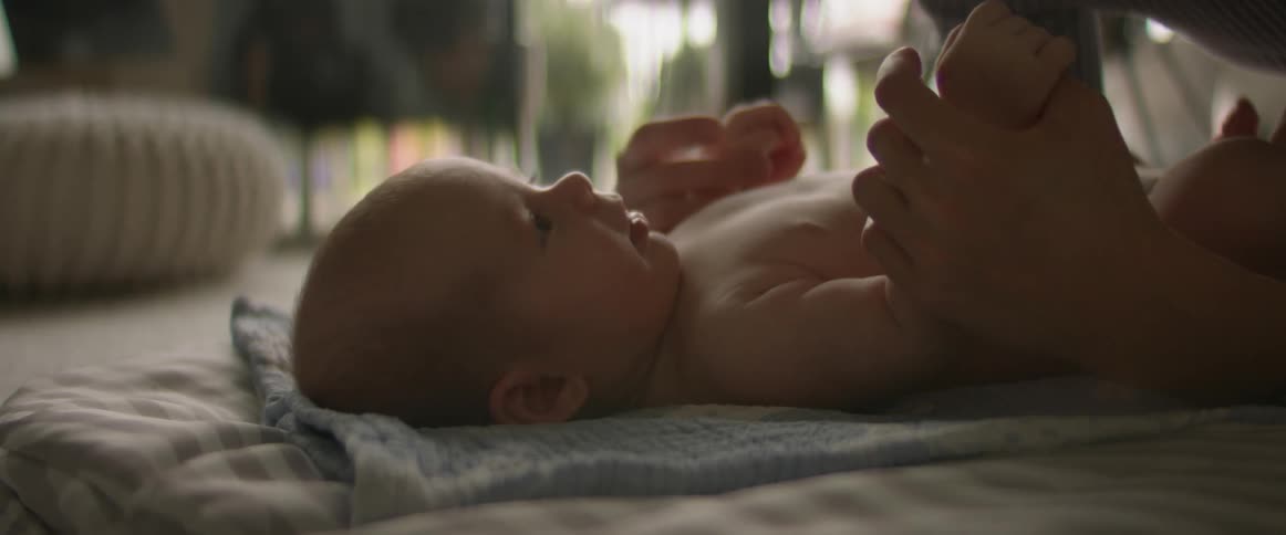 Mother with sweater holds baby with diaper lying on floor