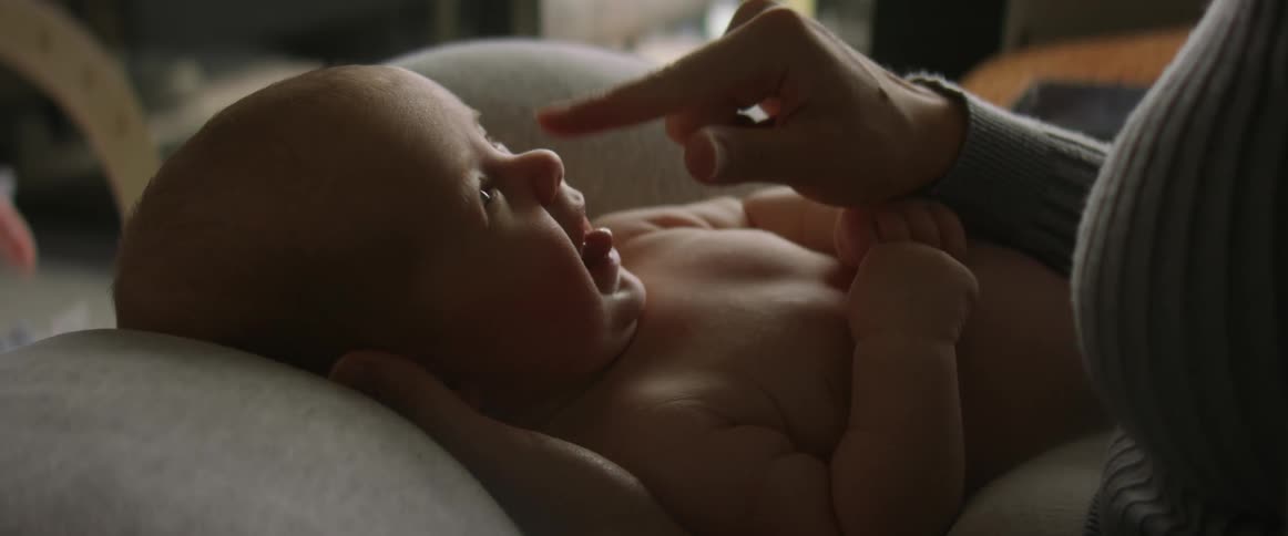 Mother teases baby in her lap by tapping the childs nose