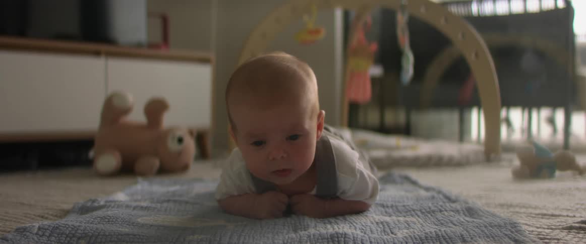 A cute young baby on its stomach holds up its head while looking forward