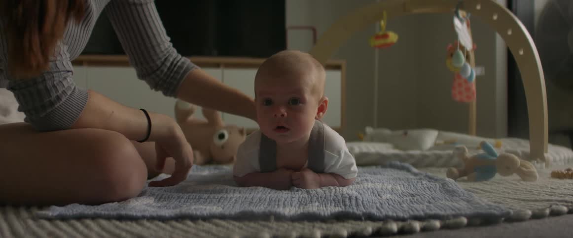 Mother leans down to kiss baby lying on blanket near mobile