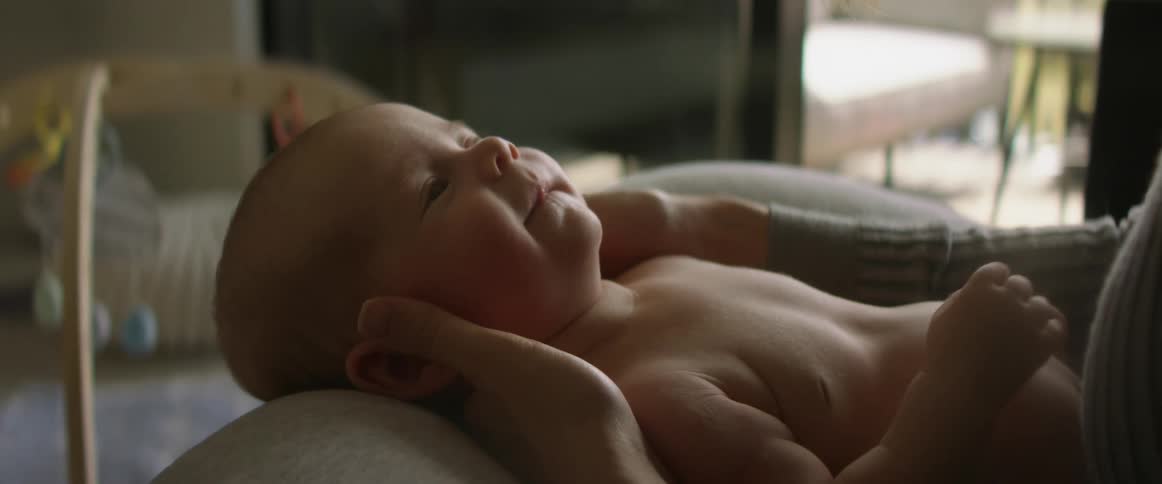 Happy baby wiggles and moves his arms while being held by his mother at home