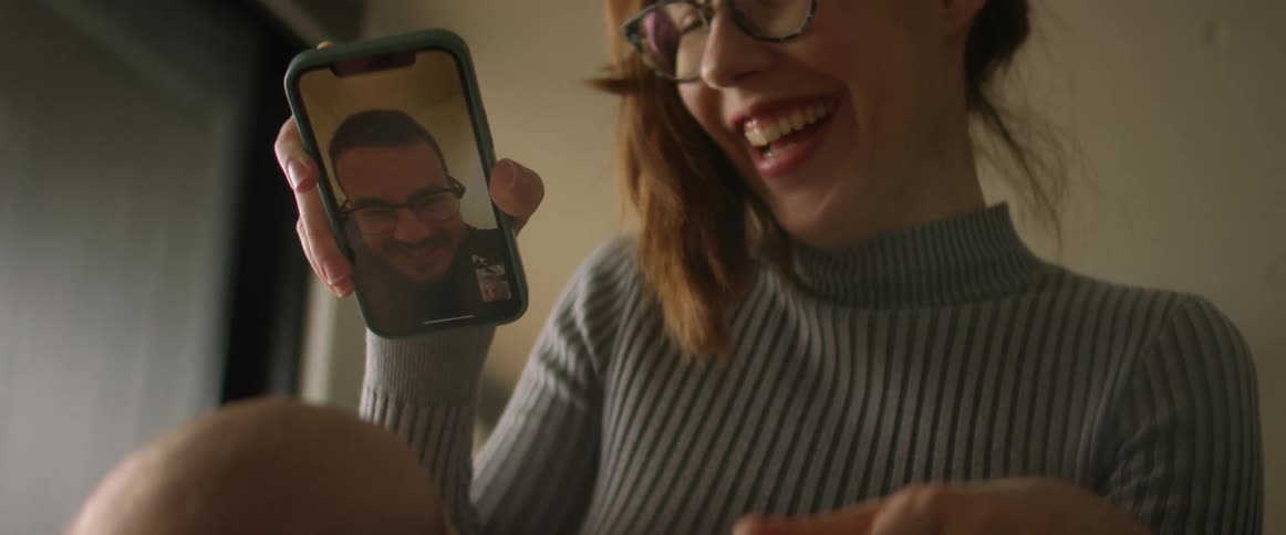 Woman sitting on couch and talking to young man on smartphone with facetime laughing and smiling