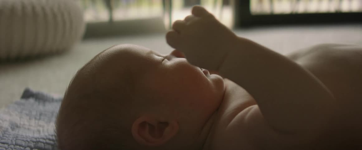 Mother plays with baby lying on blanket on the floor