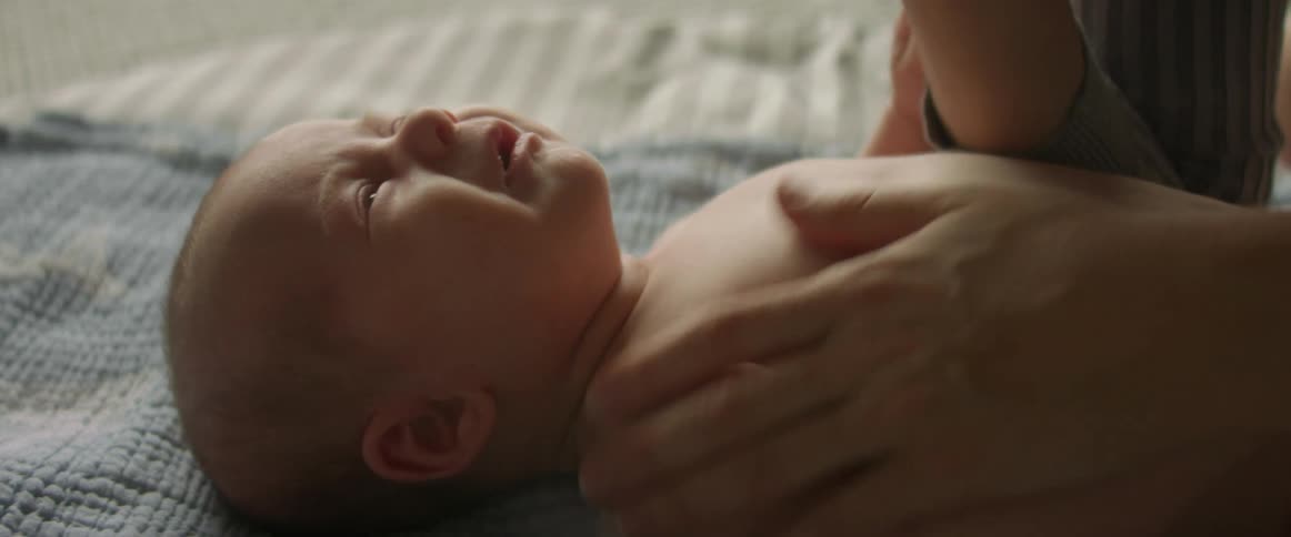A baby is lying an a blanket crying as their mother tries to comfort them