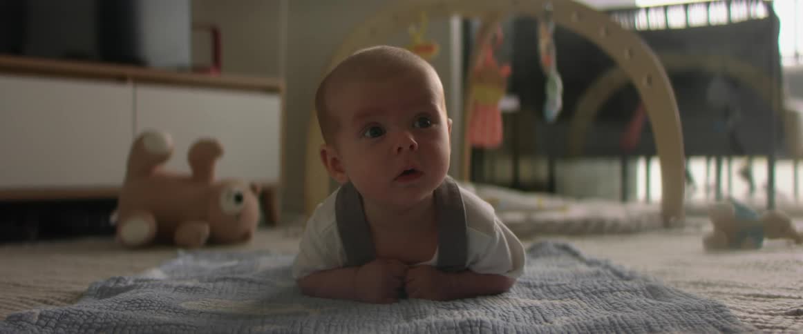 A baby is lying on a blanket on the floor surrounded by toys as he looks around