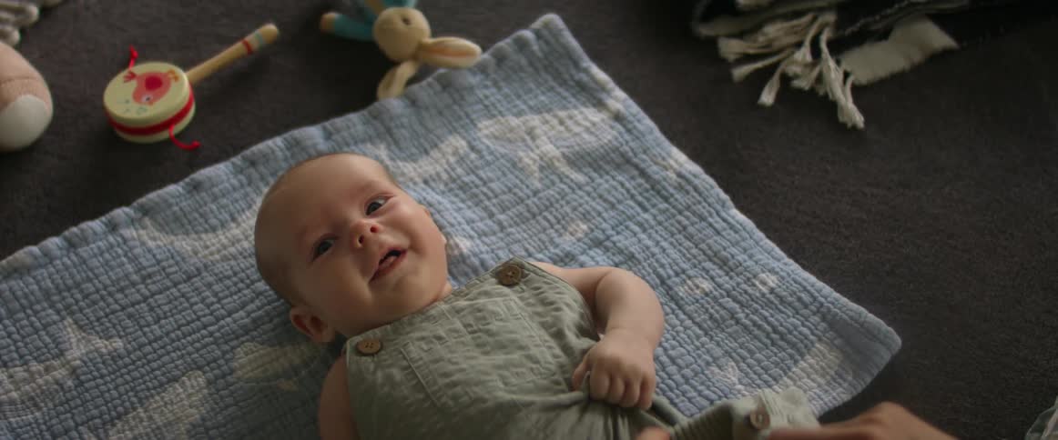 Mother dresses baby lying on the floor next to toys