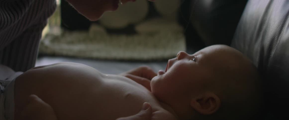 Mother leans down to touch noses with baby on couch