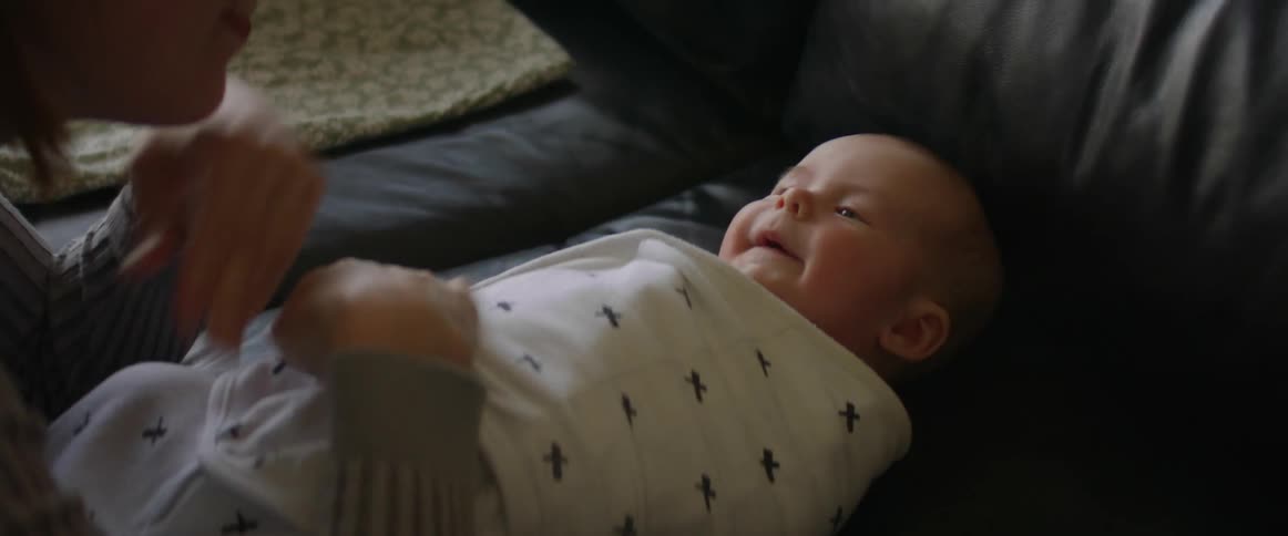 Mother bundles baby lying on couch into a thin blanket