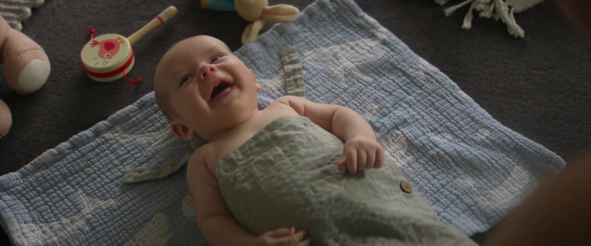 A baby laying on the floor laughing as an adult leans over him