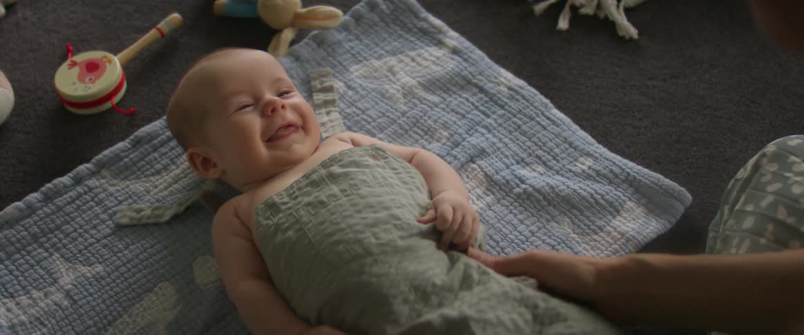 Happy baby wiggles and smiles while being held by his mother at home