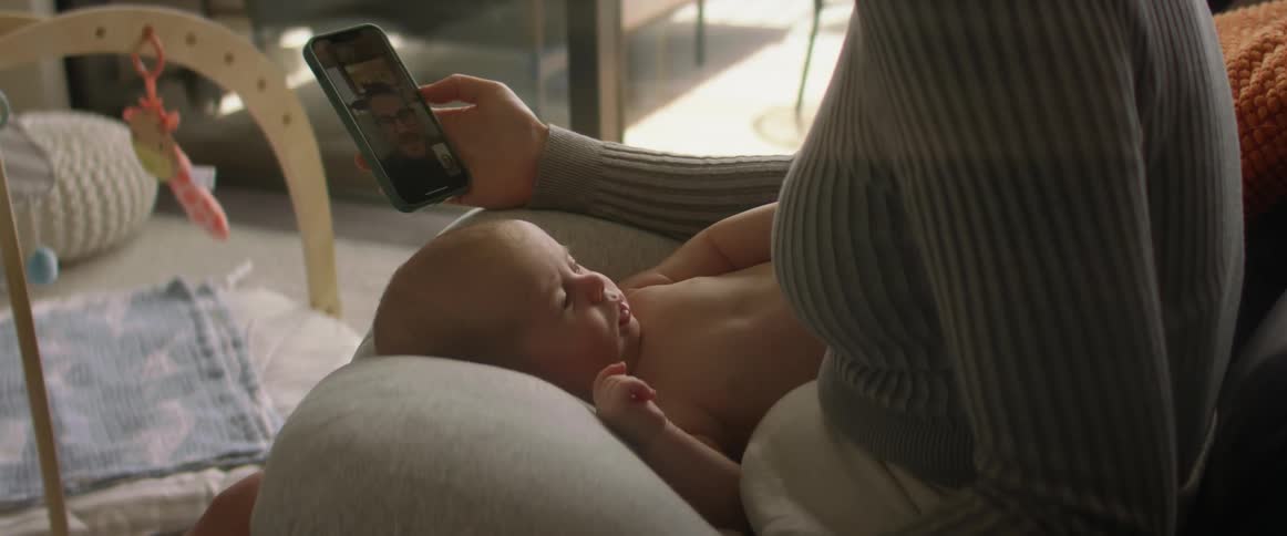 A baby laying in their mothers lap sitting on the couch as the mother is on her phone