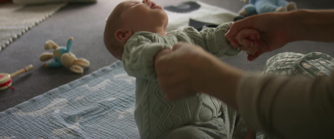 An adult pulling a baby by their arms up off the floor