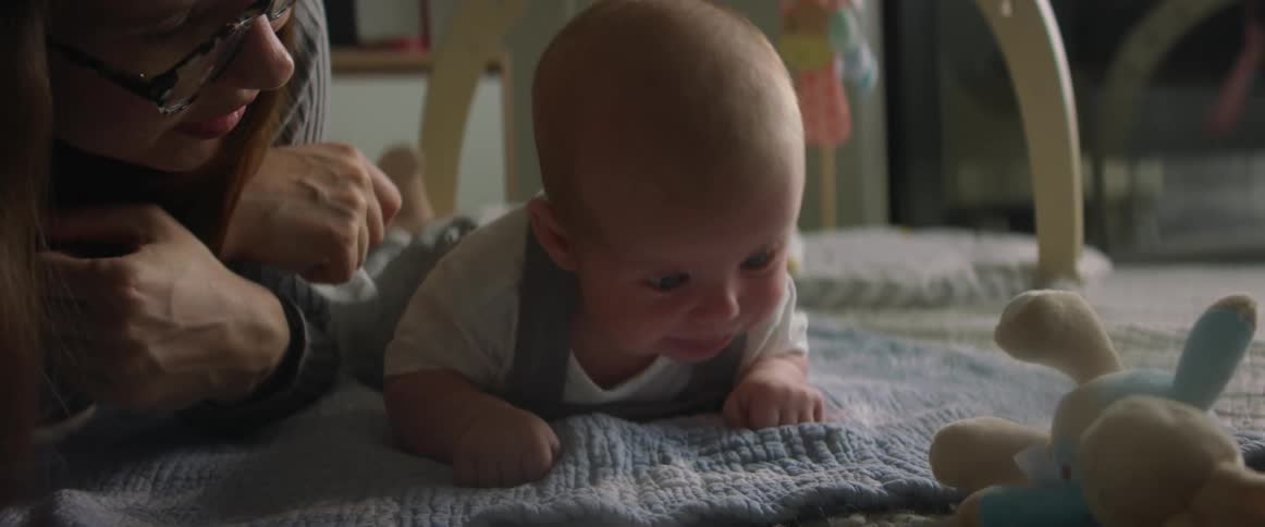 Mother rubs back and head of baby lying on a blanket on the floor