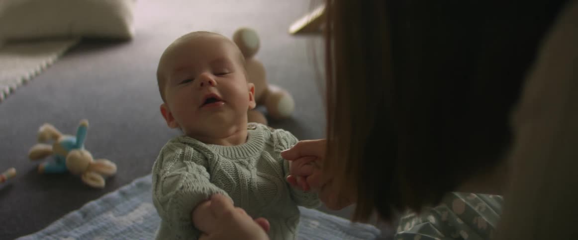 A mother holds her babys tiny arms and tries to teach him how to stand