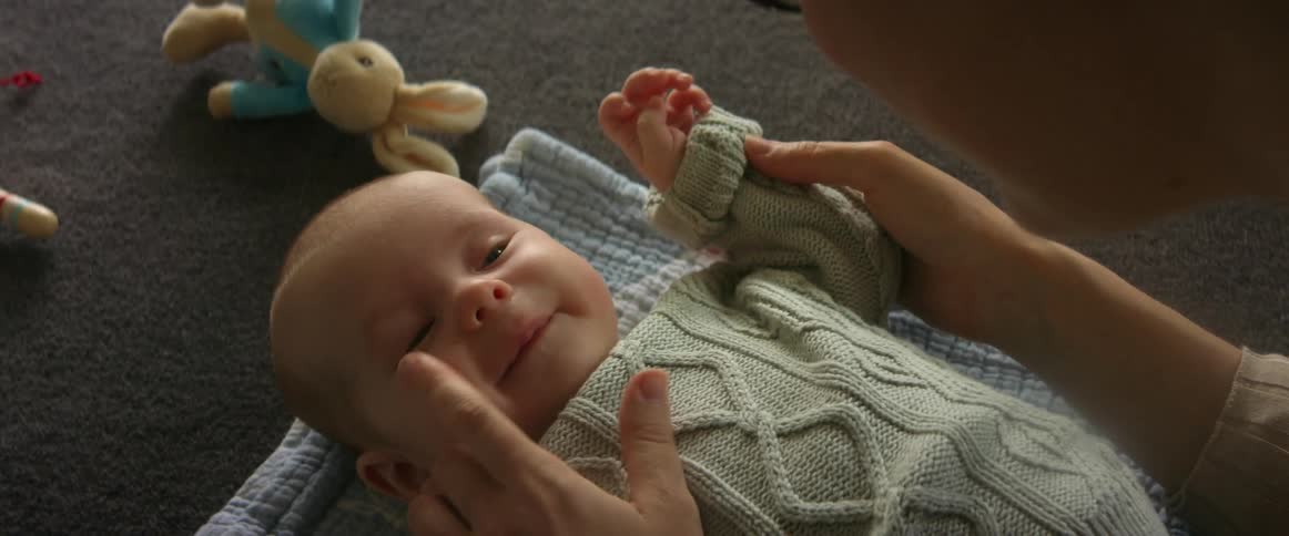 Infant lying on blanket cooing and smiling while mom plays with her