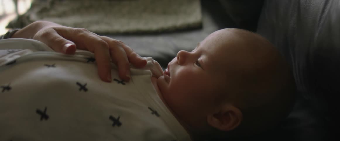 Mother wraps child lying on couch in thin blanket