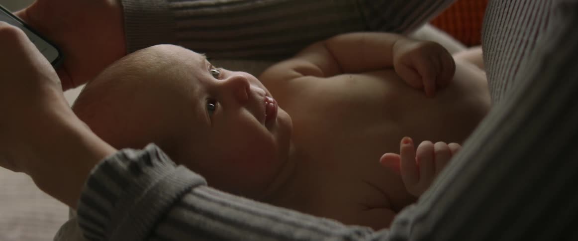 A woman scrolls through her phone while cradling her baby