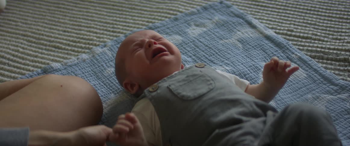 Mother kneels next to baby crying on a blanket on the floor