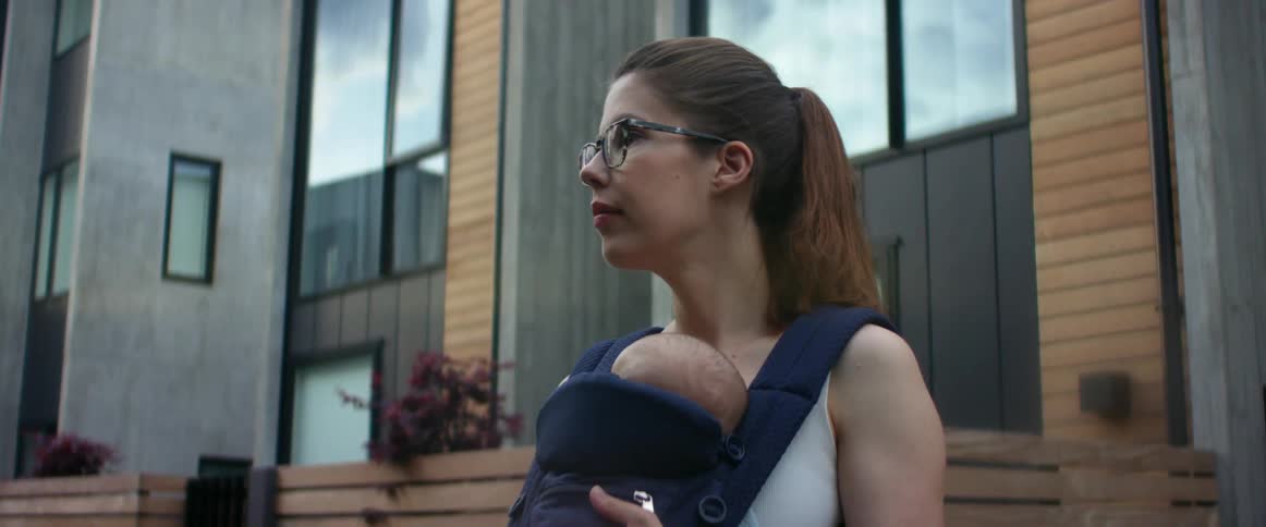 A mother holding her baby in a front carrier while she stands outside of a building