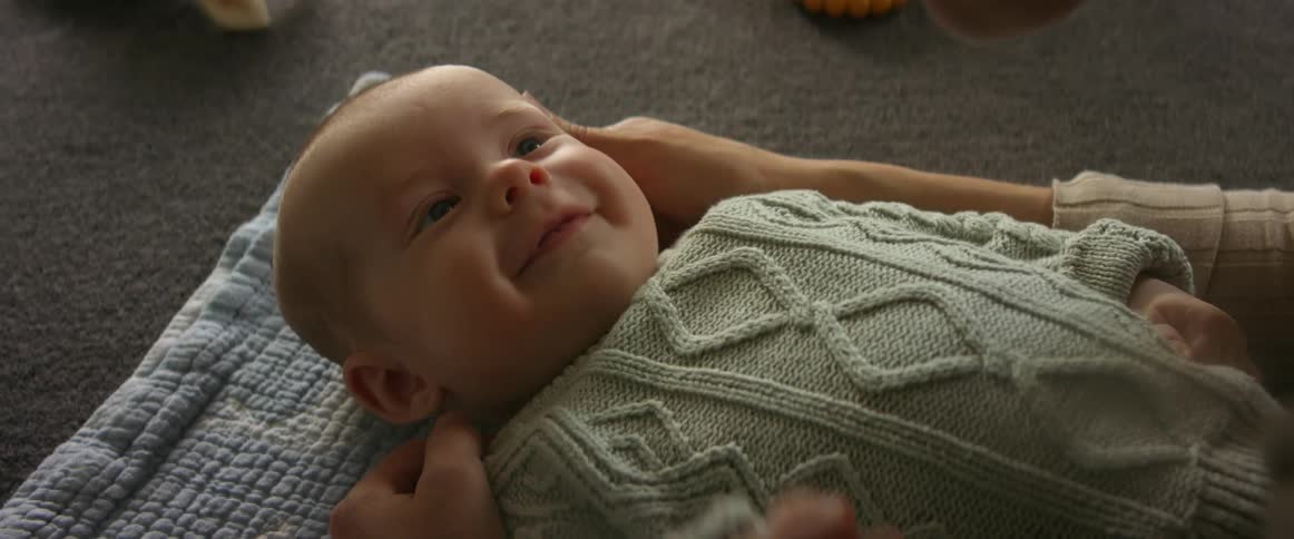 Baby son smiles and tries to touch mother looking down at him