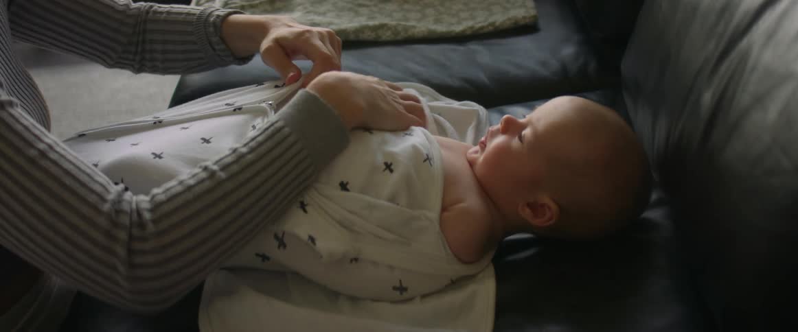 Mother zips baby lying on couch into bundle