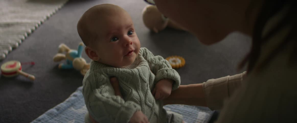 A mother holds a baby upright as the baby moves its arms around