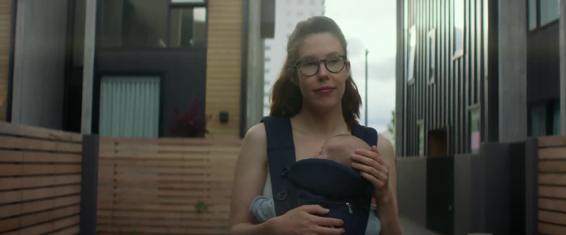 Mother carries child in baby carrier as she walks between apartment buildings