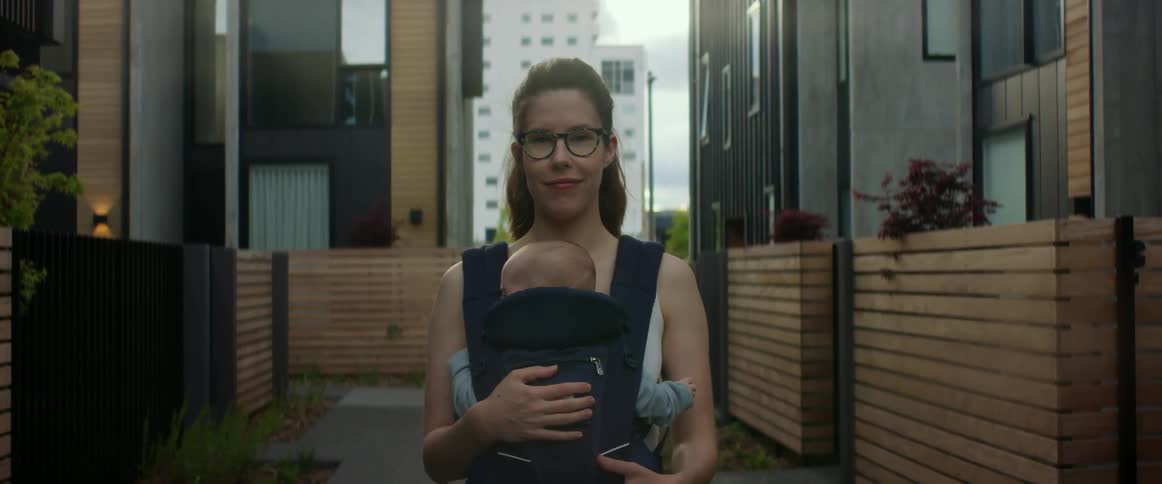 A mother has her baby in a front sling and stands facing the camera