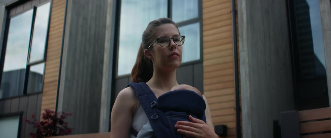 A teenage girl with a baby in a bay sling carrier resting on her chest looks down with an expression of slight regrete and hardship