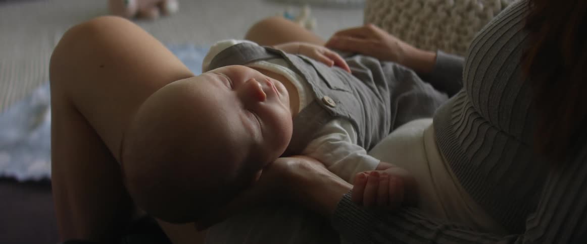 Mother with shorts and sweater holds baby son sitting on couch in the living room