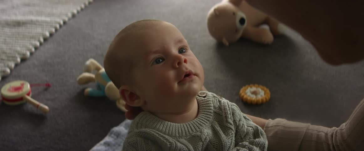 A babies face smiling as his mother holds him up right