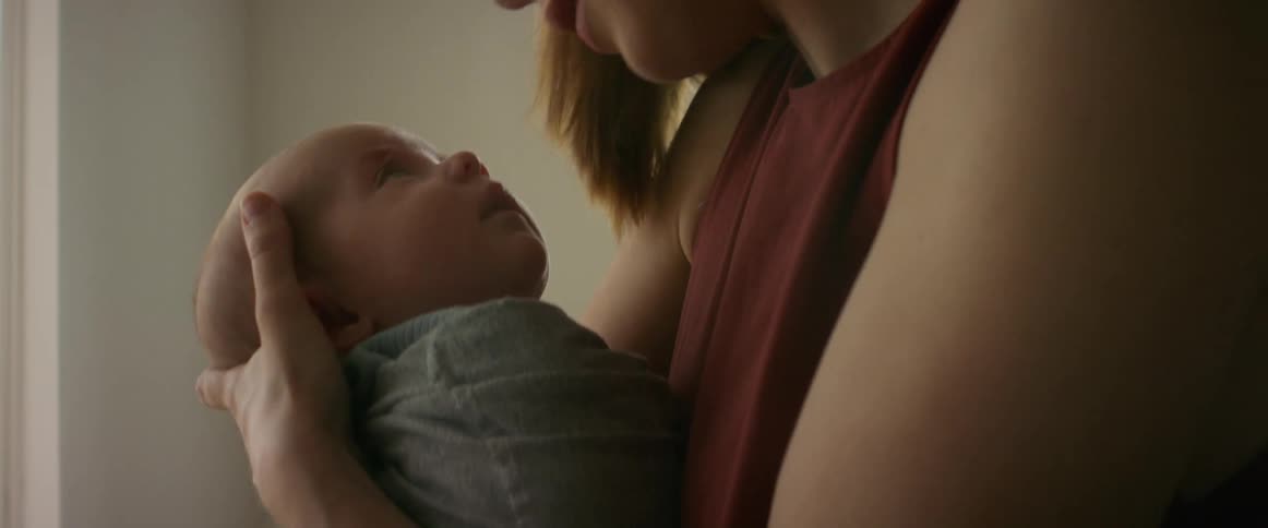 A woman kisses a newborn baby as she rocks it in her arms while standing indoors during the day
